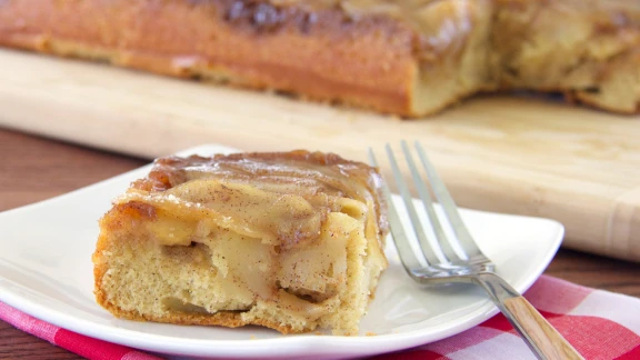 Slice of apple cake with caramelized apples on top, served on a plate