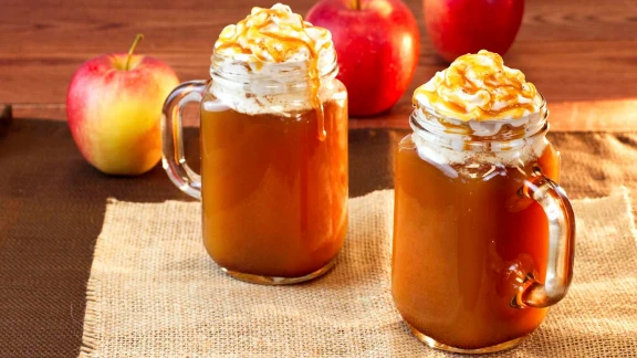 Caramel apple cider in mason jar mugs topped with whipped cream and caramel drizzle
