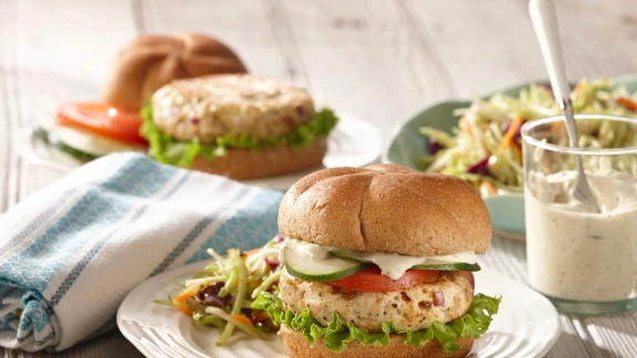 Whole grain chicken burger with lettuce, tomato, cucumber, and mayonnaise, served with a side of coleslaw and a cup of dressing.