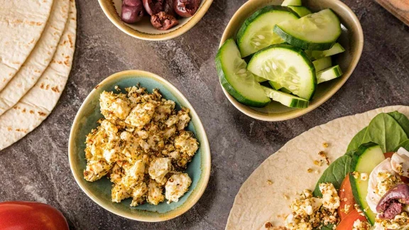 Close-up of a healthy Mediterranean-style meal with tortillas, cucumber slices, olives, crumbled feta cheese, and fresh vegetables