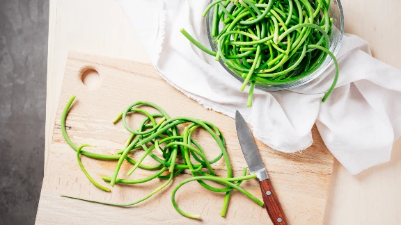 Fresh garlic scapes on cutting board with knife