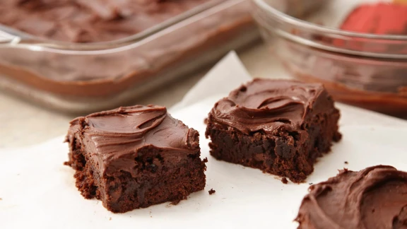 Rich chocolate brownies with creamy chocolate frosting cut into squares on parchment paper