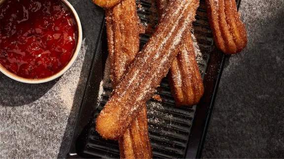 Cinnamon sugar churros served on black tray with side of strawberry dipping sauce
