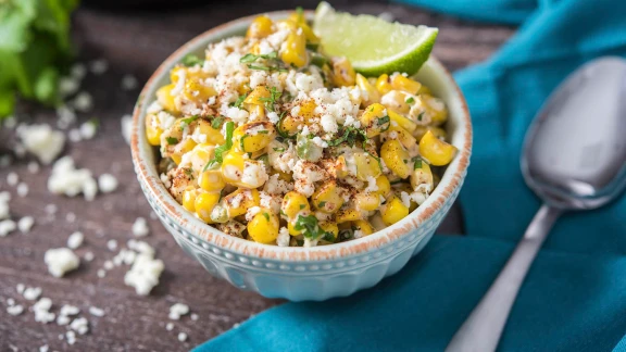 Mexican street corn esquites with cotija cheese, chili powder, cilantro, and lime wedge in ceramic bowl
