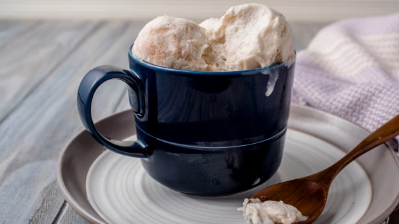 Creamy homemade ice cream served in dark blue mug on plate with wooden spoon
