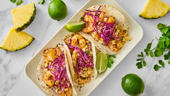 Shrimp tacos with pineapple salsa, shredded purple cabbage, and lime wedges served on flour tortillas