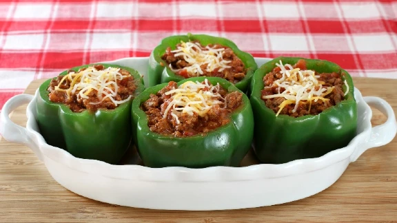 Green bell peppers stuffed with meat sauce and topped with shredded cheese in a white baking dish