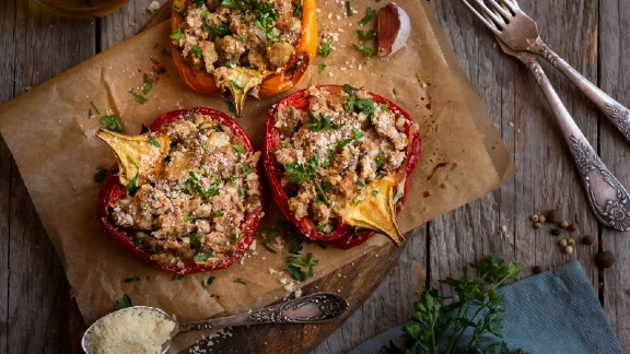Stuffed bell peppers with ground meat and herbs topped with grated cheese on parchment paper