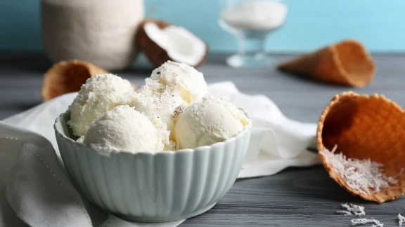 Vanilla ice cream scoops in a bowl with shredded coconut and waffle cones