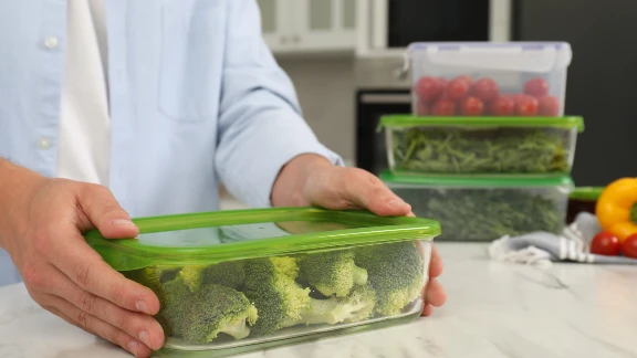 Person storing broccoli in a green-lid container