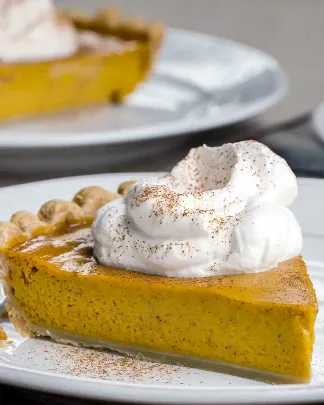 Slice of pumpkin pie topped with whipped cream and cinnamon on white plate