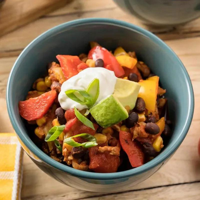 A bowl of chili with sour cream, avocado, and green onions.